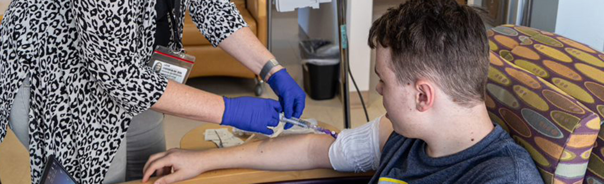 Nurse's blue-gloved hands starting the infusion as Erik looks on