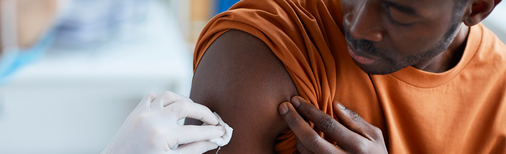 A man with his orange T-shirt sleeve rolled up gets prepped for a shot